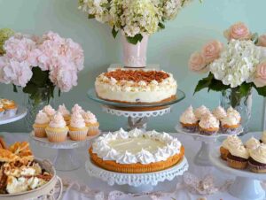 A dessert table showcasing cream cheese and white chocolate pudding mix recipes, including trifles, cheesecakes, cupcakes, and pie.
