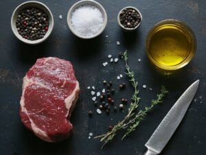 A raw beef chuck eye steak on a wooden cutting board with rosemary, garlic, and sea salt.
