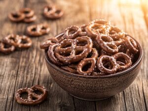 A bowl of milk chocolate covered pretzels on a wooden table with natural light.