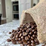 Freshly roasted coffee beans pouring onto a white marble counter.