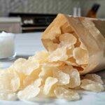 Close-up of salt and vinegar chips spilling from a bag on a white marble counter.